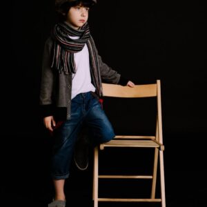A fashionable young boy posing with a chair in a studio on a dark background.