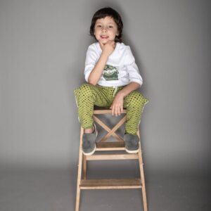 Adorable young boy sitting on a stool, smiling playfully in a studio photoshoot.