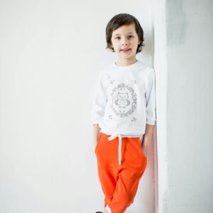 Portrait of a happy young boy posing stylishly in a white and orange outfit indoors.